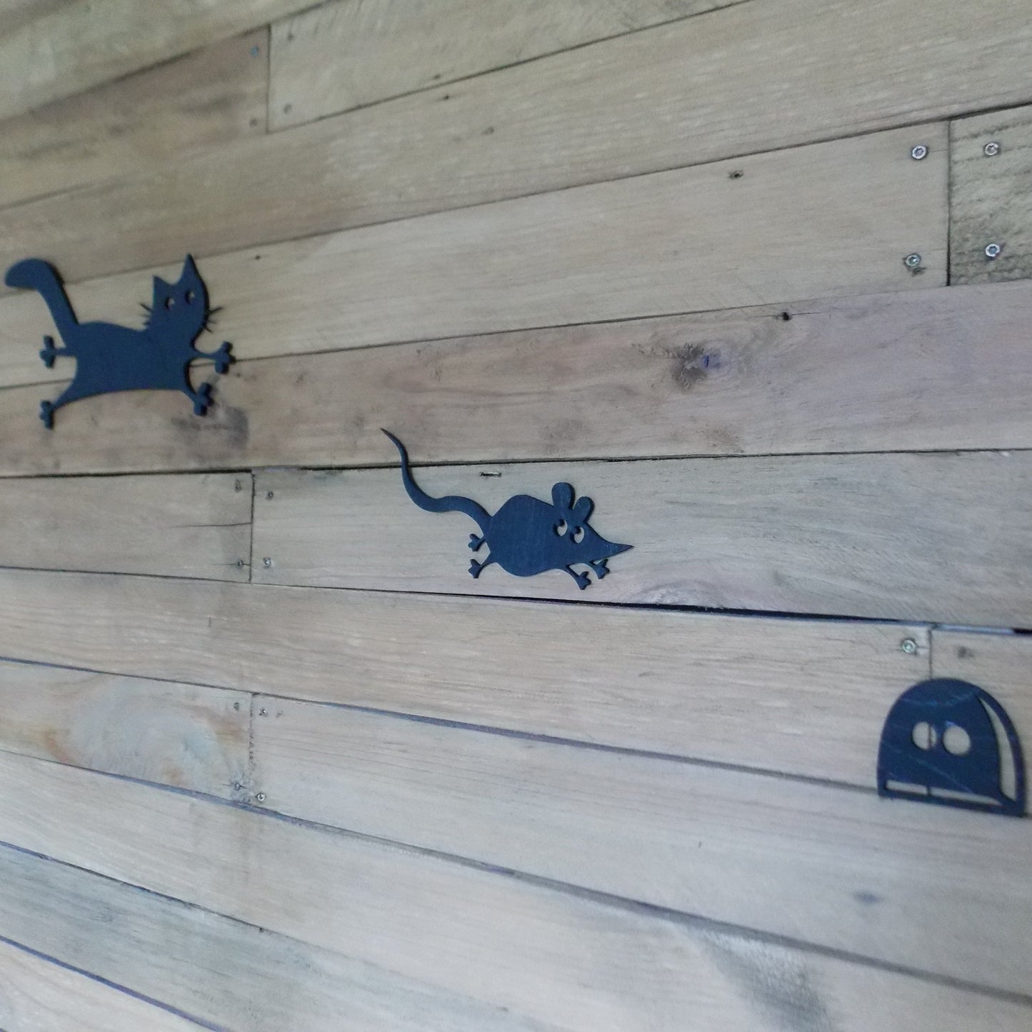 Wooden surface with blue cut-out shapes of a cat, mouse, and mouse hole.